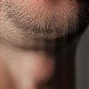 男性の顔の頬と顎のクローズアップ。光を反射して非常に滑らかで清潔な肌が強調されている。